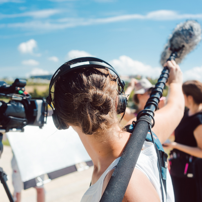 Woman,Holding,Microphone,On,A,Boom,During,Video,Production,Capturing Woman holding boom microphone at film set